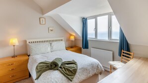 A bedroom with a bed, two bedside tables, a window with curtains, a radiator, and a wooden chair. - 2 Bed in Weymouth (oc-s42788) (Weymouth)