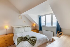 A bedroom with a bed, two bedside tables, a window with curtains, a radiator, and a wooden chair. - 2 Bed in Weymouth (oc-s42788) (Weymouth)