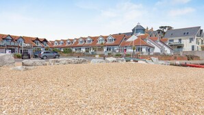 A coastal residential area with houses, a pebbled beach, and parked cars. - 2 Bed in Weymouth (oc-s42788) (Weymouth)