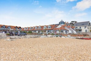 A coastal residential area with houses, a pebbled beach, and parked cars. - 2 Bed in Weymouth (oc-s42788) (Weymouth)