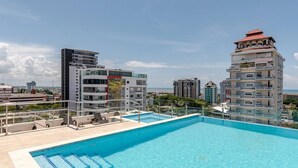 Una piscina sul tetto con acqua cristallina, circondata da edifici moderni, tra cui una struttura con un caratteristico tetto rosso.