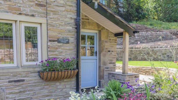 Ein Steinhaus mit einer blauen Tür, einem fensterartigen Gitter und einem Blumenkasten mit violetten Blumen.