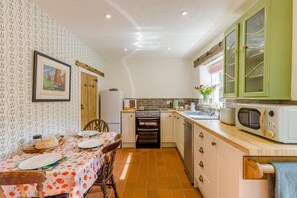 A compact kitchen with a dining area, featuring a tiled backsplash, wooden cabinets, and a small dining table set with plates and cutlery. - 2 Bed in Glossop (oc-h43766) (Glossop)