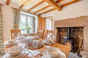 A dining area with a table set for four, a fireplace, wooden beams, and a window with curtains. - 3 Bed in Whatstandwell (oc-h42743) (Whatstandwell)