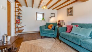 Een gezellige woonkamer met een houten plafond, een blauwgroene bank, een fauteuil, een boekenkast en een raam.