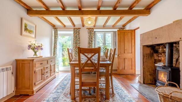 Een eethoek met een houten tafel en stoelen, een open haard en uitzicht door een raam.