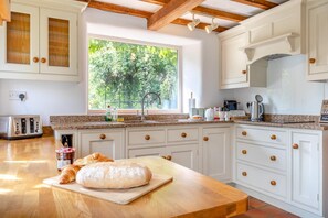 A kitchen with a large window, wooden cabinets, a granite countertop, and a wooden table with bread. - 3 Bed in Whatstandwell (oc-h42743) (Whatstandwell)