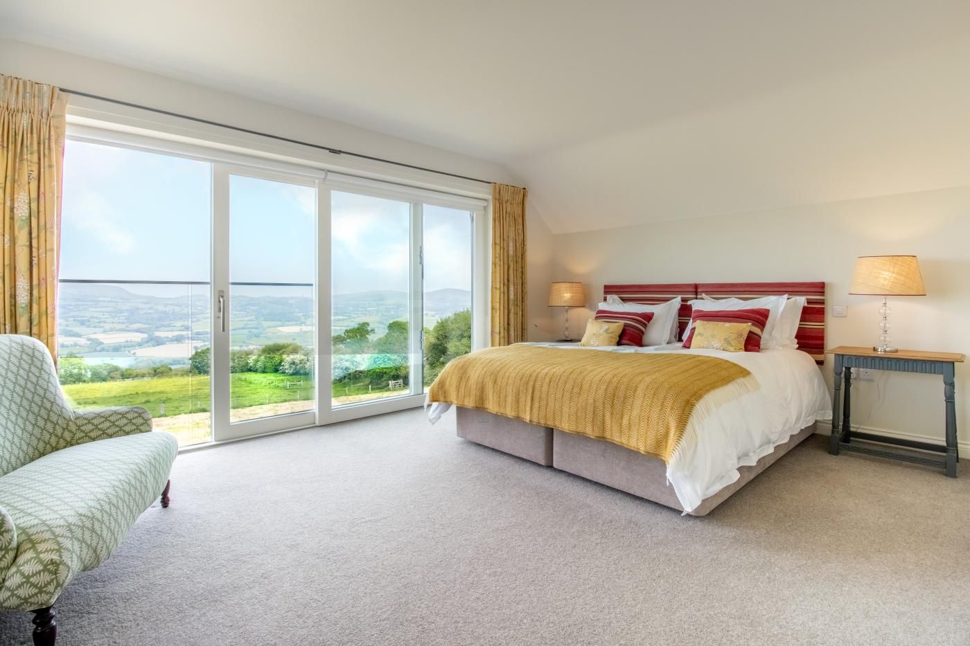 A bedroom with a bed, a chair, a nightstand, and a view of the outdoors.