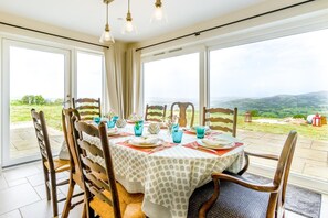 A dining area with a table set for four, surrounded by chairs, large windows with a view of the countryside, and pendant lighting. - 4 Bed in Banks Head (oc-h43280) (Bishop's Castle)