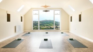 Ein Yoga-Raum mit großen Fenstern, Holzboden und Deckenventilator.