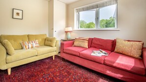 Ein Wohnzimmer mit zwei Sofas, einem gemusterten Teppich, einem Fenster mit Blick und einer Lampe auf einem Beistelltisch.