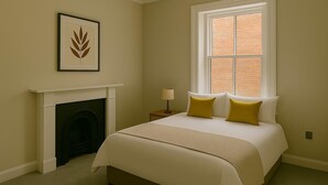 Een slaapkamer met een bed, een open haard, een raam en een ingelijst kunstwerk aan de muur.