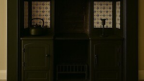 A dark-colored cabinet with two windows, each with a patterned curtain.