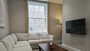 A living room with a beige sofa, a wooden coffee table, a flat-screen TV mounted on the wall, and a window with curtains. - 3 Bed in Carlisle (oc-a42763) (Carlisle)