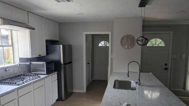 A kitchen with white cabinets, a stainless steel refrigerator, a microwave, a gas stove, and a sink. - Spacious 4BR Home · Near IAH · Self Check-In (Spring)