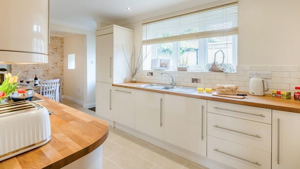 A modern kitchen with white cabinets, a wooden countertop, a built-in oven, and a window with blinds. - 3 Bed in Scalby (oc-s42779) (Scalby)