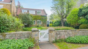 A residential area with stone walls, a white gate, and a house with a tiled roof. - 3 Bed in Scalby (oc-s42779) (Scalby)