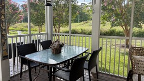 Une terrasse couverte avec une table en verre, des chaises en osier noir et une jolie nichoir décoratif en guise de centre de table.