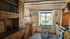 Une cuisine avec des meubles en bois, une table à manger avec des chaises, une fenêtre donnant sur un beau paysage et un sol carrelé.