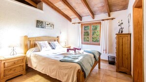 Un dormitorio con cama de madera, mesita de noche, armario y ventana con vista a la vegetación.