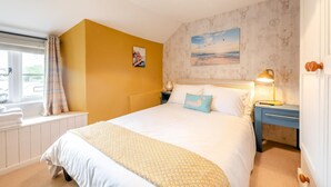 A bedroom with a bed, bedside tables, a window with curtains, a radiator, and a wall with a painting. - 3 Bed in Wrafton (oc-t44230) (Braunton)