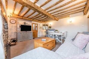 Ein gemütliches Wohnzimmer mit Holzbalkendecke, einem Fernseher, einem Essbereich mit Stühlen und einem Sofa.