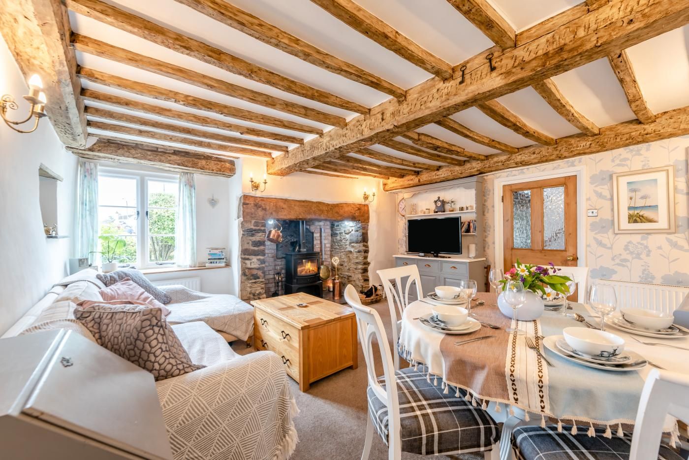 Een gezellige woonkamer met een open haard, een eethoek met een tafel gedekt voor twee personen, en een bank met decoratieve kussens.