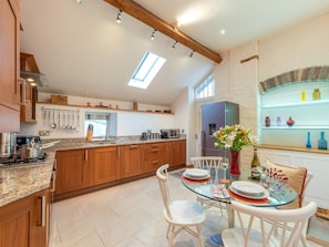 A modern kitchen with wooden cabinets, a granite countertop, a dining area with a glass table, and a built-in wine rack. - 1 Bed in Brecon (oc-42936) (Llanfrynach)