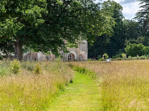 A pathway leading to a historic building with arched windows and a stone facade, surrounded by a field and trees. - 1 Bed in Brecon (oc-42936) (Llanfrynach)