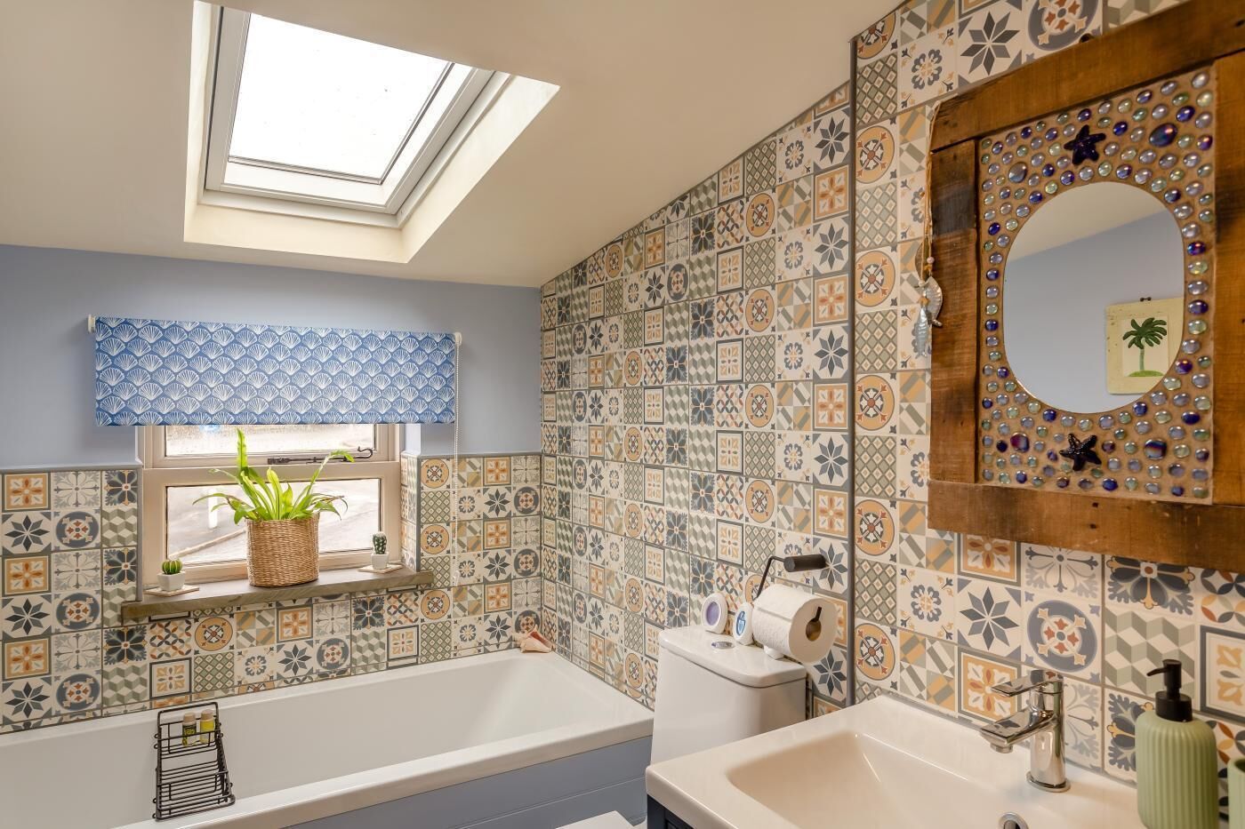 Une salle de bain dotée d’un puits de lumière, de carreaux décoratifs, d’une baignoire, de toilettes et d’un miroir agrémenté d’éléments décoratifs.