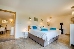 A bedroom with a bed, bedside tables, a wall-mounted lamp, a painting, and a fireplace. - 3 Bed in Duntisbourne Abbots (oc-f42787) (Duntisbourne Abbots)
