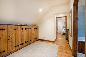 A hallway with wooden cabinets, a carpeted floor, and a bedroom with a bed and a window. - 3 Bed in Duntisbourne Abbots (oc-f42787) (Duntisbourne Abbots)
