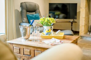 A wooden table with a metal pitcher, two wine glasses, a vase with yellow flowers, and a box with a phone. - 3 Bed in Duntisbourne Abbots (oc-f42787) (Duntisbourne Abbots)