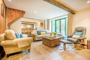 A cozy living room with a wooden staircase, a dining area, and a view through large windows. - 3 Bed in Duntisbourne Abbots (oc-f42787) (Duntisbourne Abbots)