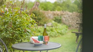 Ein runder Metalltisch mit einer Weinflasche, einer Schüssel und einer Tasse in einem Garten.