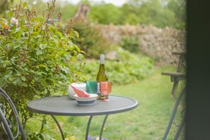 A round metal table with a bottle of wine, a bowl, and a cup in a garden setting. - 3 Bed in Duntisbourne Abbots (oc-f42787) (Duntisbourne Abbots)