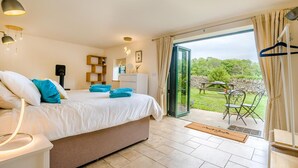 Ein Schlafzimmer mit einem Bett, Nachttischlampen, einem Schminktisch, einem Spiegel und Blick auf einen Garten durch eine Glastür.