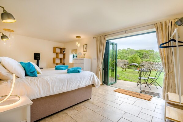 Une chambre à coucher comprenant un lit, des lampes de chevet, une commode, un miroir et une vue sur un jardin, visible à travers une porte vitrée.