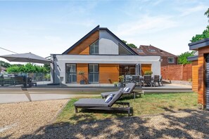 Ein modernes, zweistöckiges Haus mit einer Terrasse, Sitzgelegenheiten im Freien und einem Swimmingpool.