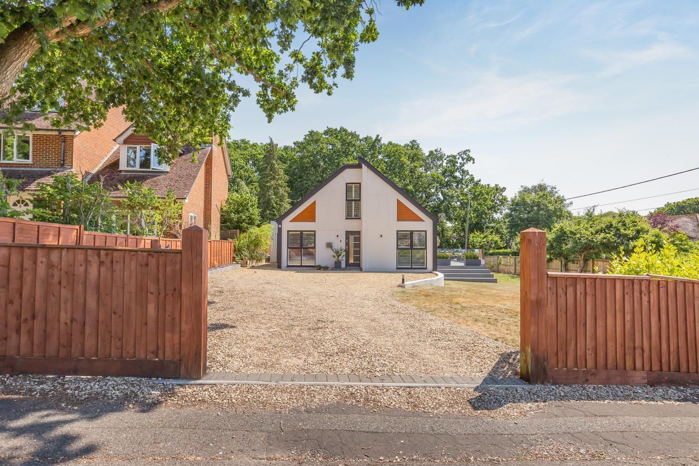 A modern two-story house with a gravel driveway and wooden gates.