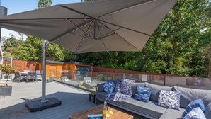 A patio with a wooden table, a sofa with patterned cushions, and a large umbrella. - 4 Bed in New Milton (oc-b44761) (New Milton)