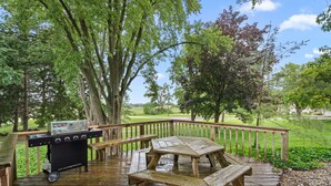 A wooden deck with a barbecue grill and picnic table, surrounded by trees and a view of a golf course.
