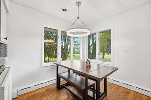 A dining area with a wooden table, large windows, and a hanging light fixture.