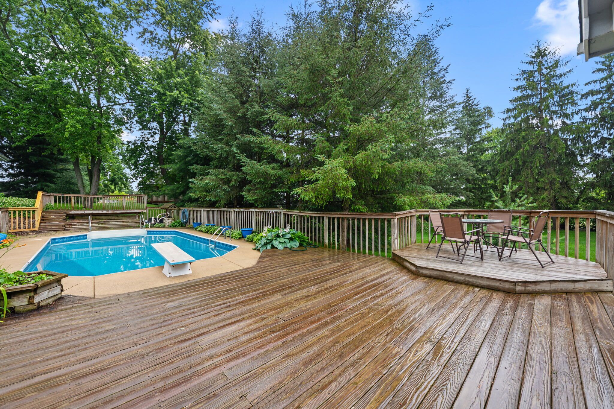 A wooden deck with a pool, surrounded by trees and a deck chair.