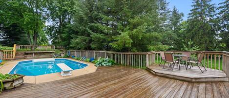 A wooden deck with a pool, surrounded by trees and a deck chair.