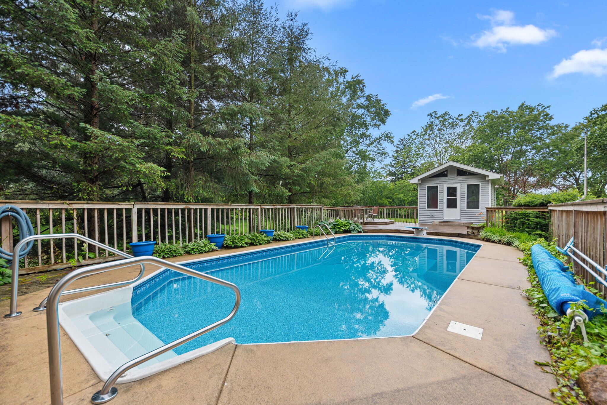 A rectangular swimming pool with a metal ladder, surrounded by a wooden deck and a metal fence.