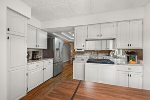 A kitchen with white cabinets, a wooden floor, and a central island. - Creekside Lodge Retreat - Pool, Billiards & Arcade (Baroda)