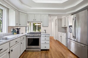 A modern kitchen with white cabinetry, stainless steel appliances, and a view to the outdoors.