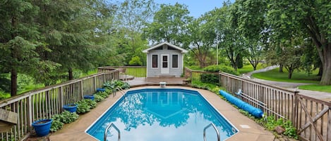 A rectangular pool with a wooden deck, surrounded by a wooden fence, and a small building in the center.