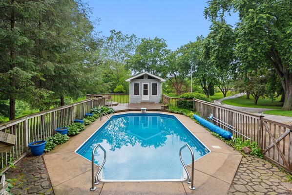 Une piscine rectangulaire dotée d’une terrasse en bois, entourée d’une clôture en bois, et un petit bâtiment situé au centre.